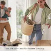 A woman is holding a breast pump and a basket, while a man holds a baby in the background. A baby stroller is on the floor. Produktbild-Vorschau