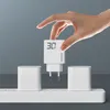 A hand is holding a white USB charger above a white power strip with two other white chargers plugged in. Podgląd zdjęcia produktu
