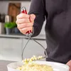A person is using a potato masher to mash potatoes in a white bowl in a kitchen. Produktbild-Vorschau