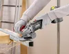 A person wearing gloves is using a cordless angle grinder to cut a metal pipe. Produktbild-Vorschau