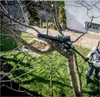 A person is using a telescopic pole saw to trim branches from a tree. Podgląd zdjęcia produktu