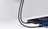 Two smartphones are being charged by a black USB cable plugged into a wall charger. Produktbild-Vorschau