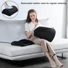 A woman sitting on a couch, holding a black cushion while another black cushion is on the couch. Produktbild-Vorschau