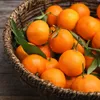 A close-up shot of a woven basket filled with fresh mandarins and green leaves, set against a rustic wooden background. Produktbild-Vorschau