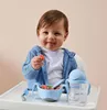 A baby sitting in a high chair, eating from a blue bowl and drinking from a blue bottle. Náhled obrázku produktu