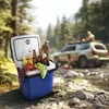 A blue cooler box filled with drinks and fruit is placed outdoors next to a stream, with people and a car in the background. Náhled obrázku produktu
