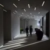 Two people walk down a modern office hallway with linear lights on the ceiling and shadows cast on the floor. Anteprima dell’immagine prodotto