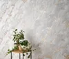 A close-up of a textured wallpaper with a marble-like pattern, featuring two potted plants and a wooden bird figurine on a small table in the foreground. Podgląd zdjęcia produktu