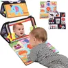 A baby is playing with a soft fabric activity mat and book. Produktbild-Vorschau