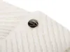 A close-up of a white knitted accessory with a metallic logo. Produktbild-Vorschau