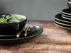 A close-up shot of black stoneware plates and bowls with gold trim, set on a wooden table. Náhľad obrázku produktu
