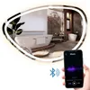 A modern bathroom with a freestanding bathtub, a toilet, and a vanity area, reflected in a large, illuminated mirror. A smartphone is shown in the foreground, connected via Bluetooth to the mirror. Produktbild-Vorschau