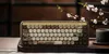 A mechanical keyboard is placed on a wooden tray next to a cup of tea and a flowering branch. Produktbild-Vorschau