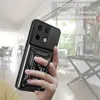 A hand holding a black phone case with a ring holder, in a bright, modern interior setting. Produktbild-Vorschau