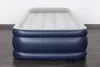 A blue and gray inflatable mattress is shown on a dark wooden floor against a white wall. Náhled obrázku produktu