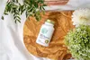 A bottle of supplements is placed on a wooden board, surrounded by greenery and a white flower. Produktbild-Vorschau