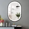 A modern oval mirror with LED lighting is displayed on a gray wall above a dark console table with decorative items. Produktbild-Vorschau