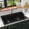A black double basin kitchen sink with a chrome faucet is shown in a well-lit kitchen setting, with a window and kitchen accessories in the background. Anteprima dell’immagine prodotto
