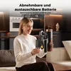 A woman is holding a cordless vacuum cleaner and its battery in a modern kitchen/living room setting. Produktbild-Vorschau