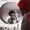 A man is trimming his hair in front of a mirror in a bathroom. Produktbild-Vorschau