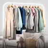 A clothing rack with various garments hanging on it, set against a neutral background with some furniture and decor visible. Náhled obrázku produktu