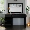 A black vanity table with gold accents is shown in a well-lit room with a large mirror above it. Decorative items and plants are placed around the table. Náhled obrázku produktu