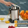A person's hand is pressing down on the handle of a stainless steel citrus juicer, with juice flowing into a glass. Oranges and mangoes are in a basket to the right, and cherries are at the bottom. Náhľad obrázku produktu