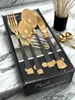 A set of gold and black cutlery is displayed on top of its packaging, which is placed on a marble surface. Produktbild-Vorschau