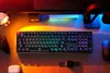 A gaming setup with a keyboard, controller, headphones, and other accessories illuminated by colorful LED lights. Produktbild-Vorschau