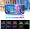 A digital alarm clock with a mirrored surface and RGB LED display, shown in a bedroom setting with a child sitting behind it. The clock has atmospheric lighting at the bottom and multiple color options are displayed in a grid below. Náhled obrázku produktu