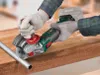 A person wearing gloves is using a cordless angle grinder to cut a metal pipe on a wooden surface. Produktbild-Vorschau