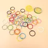 A collection of colorful metal binder rings scattered on a light peach background, with two decorative lemon slices in the upper right corner. Produktbild-Vorschau