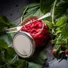 A jar of raspberries with a fork, surrounded by raspberry leaves and branches. Produktbild-Vorschau
