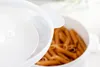 A close-up shot of a white microwave container filled with penne pasta, with the transparent lid partially open. Produktbild-Vorschau