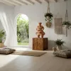 A bright, airy room with a large arched window overlooking a garden. The room features natural materials and bohemian decor, including plants, macrame wall hangings, and floor cushions. A wooden pedestal displays a decorative terracotta sculpture. Náhled obrázku produktu