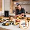 A chef is posing behind a kitchen counter filled with various dishes and a Philips Airfryer. Produktbild-Vorschau