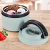 A mint green thermos with a black lid and handle, filled with ice cream and berries, sits on a wooden table next to a strawberry. Voir les images du produit