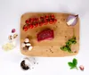 A wooden cutting board with ingredients for cooking, including a piece of raw meat, cherry tomatoes, mushrooms, onion, garlic, parsley, and spices. Produktbild-Vorschau