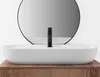 A white oval countertop sink with a black faucet is shown in front of a round mirror. Náhled obrázku produktu