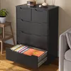 A black dresser with several drawers, one of which is pulled out to reveal colorful folders or binders inside. A plant in a white pot sits on a wooden stool to the left, and part of a gray sofa is visible on the right. Podgląd zdjęcia produktu