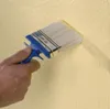 A hand is holding a paintbrush and applying a textured coating to a wall. Produktbild-Vorschau