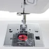 A close-up view of the needle and bobbin area of a white sewing machine. Produktbild-Vorschau