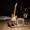 A wooden model of an electric guitar and amplifier on a wooden surface with a book and antique telephone in the background. Voir les images du produit