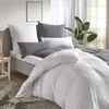 A neatly made bed with white and gray bedding, pillows, and a duvet, set in a bedroom with natural light coming from a window. Produktbild-Vorschau