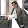 A woman leans on a railing, holding a green toiletry bag. Produktbild-Vorschau