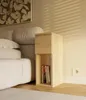A bedside table with books next to a bed, with blinds casting shadows on the wall. Anteprima dell’immagine prodotto