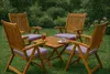A wooden garden furniture set with purple cushions, set up on a lawn with greenery in the background. Produktbild-Vorschau