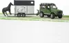 A toy Land Rover Defender towing a horse trailer with a toy horse standing next to it. Produktbild-Vorschau