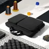 A black laptop bag is displayed on a white and black surface, surrounded by various materials like spools of thread, a plastic bottle, and foam padding. Produktbild-Vorschau