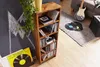 A wooden CD shelf filled with CDs and books, placed next to a chalkboard with chalk drawings. A vinyl record is on the floor in front of the shelf. In the background, a guitar and amplifier are visible. Anteprima dell’immagine prodotto
